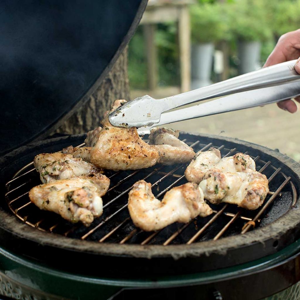 Chicken wings with tongs grilled on Big Green Egg Cast Iron Grid