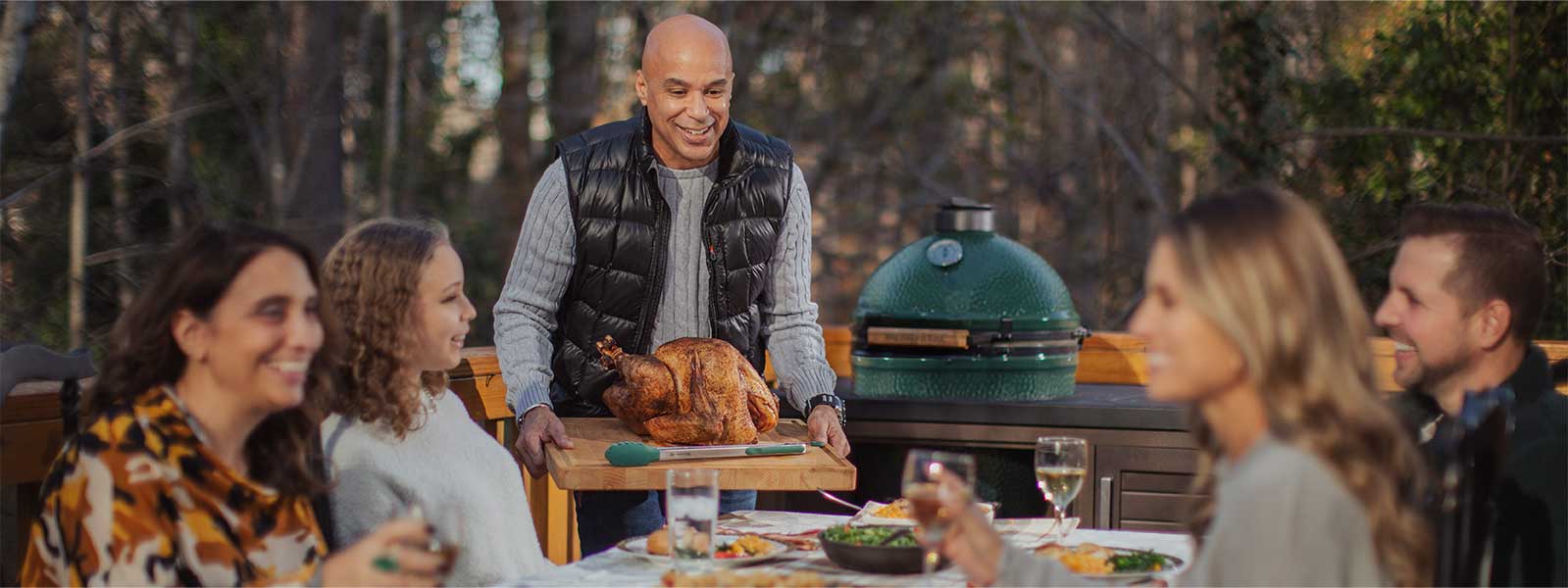 Family sitting around and outside table with the large EGG in the background from Thanksgiving